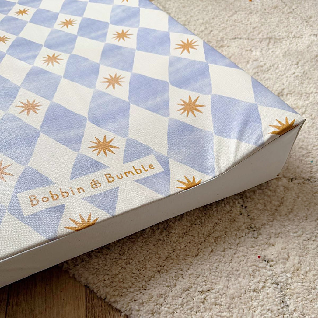 wedge baby changing mat with geometric pattern and 'Bobbin & Bumble' branding on a carpeted floor.