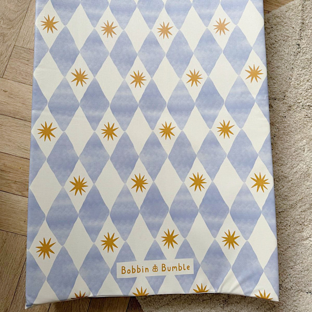 Wedge baby changing mat with blue and white diamond pattern and yellow stars on a wooden floor.