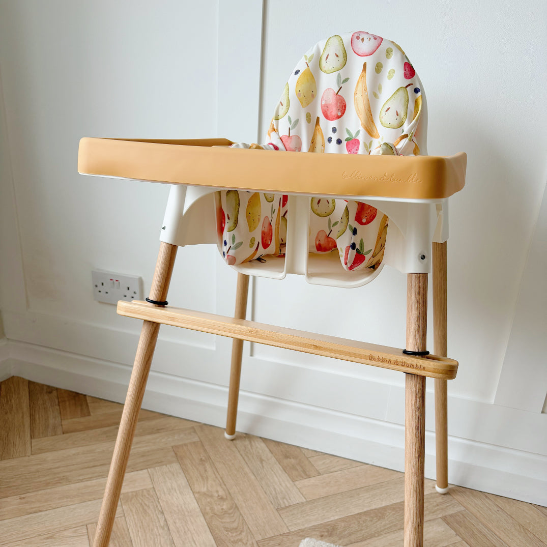 Wooden high chair with colorful seat cover on a wooden floor.