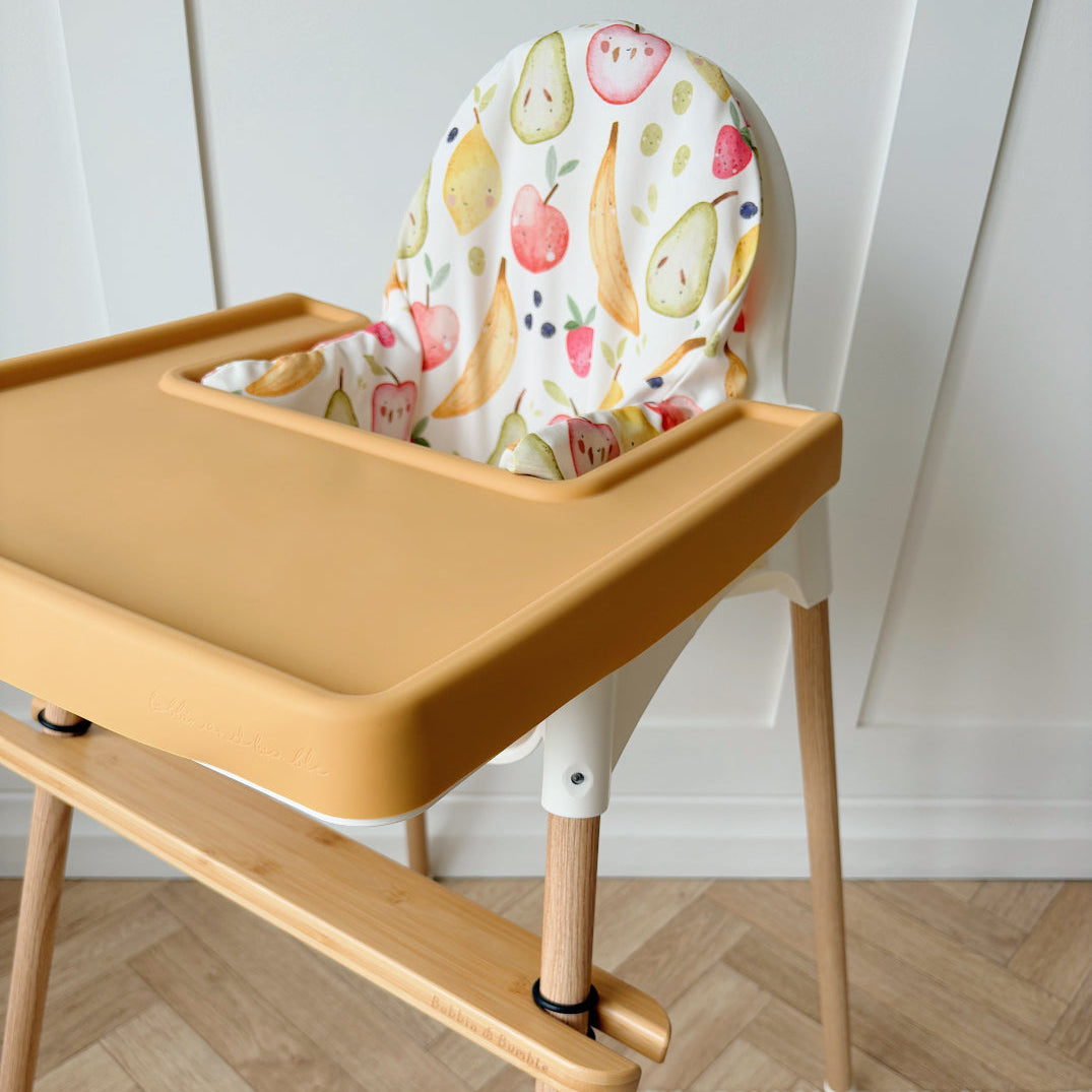 Wooden high chair with a colorful fruit-patterned cushion on a wooden floor.
