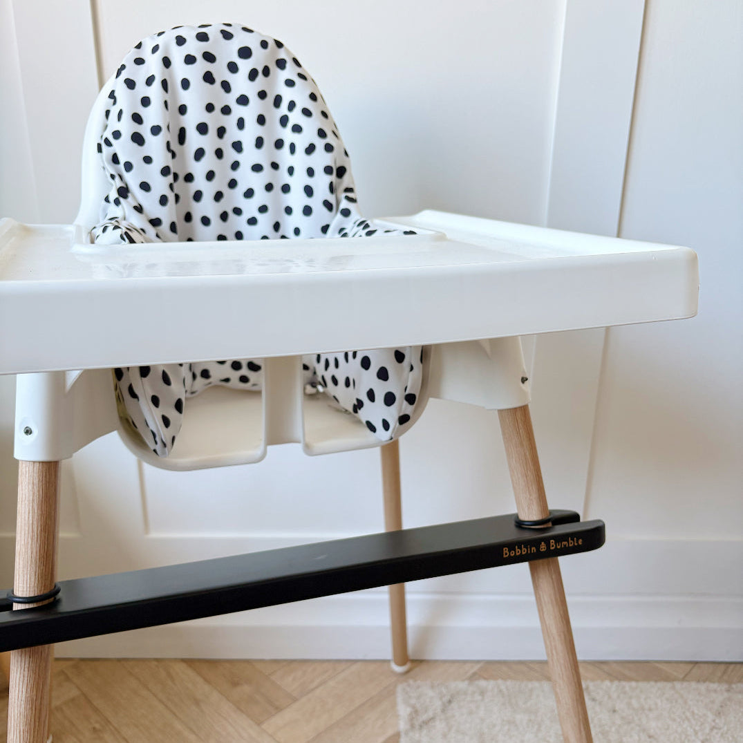 White high chair with black and white polka dot cushion on a wooden floor.