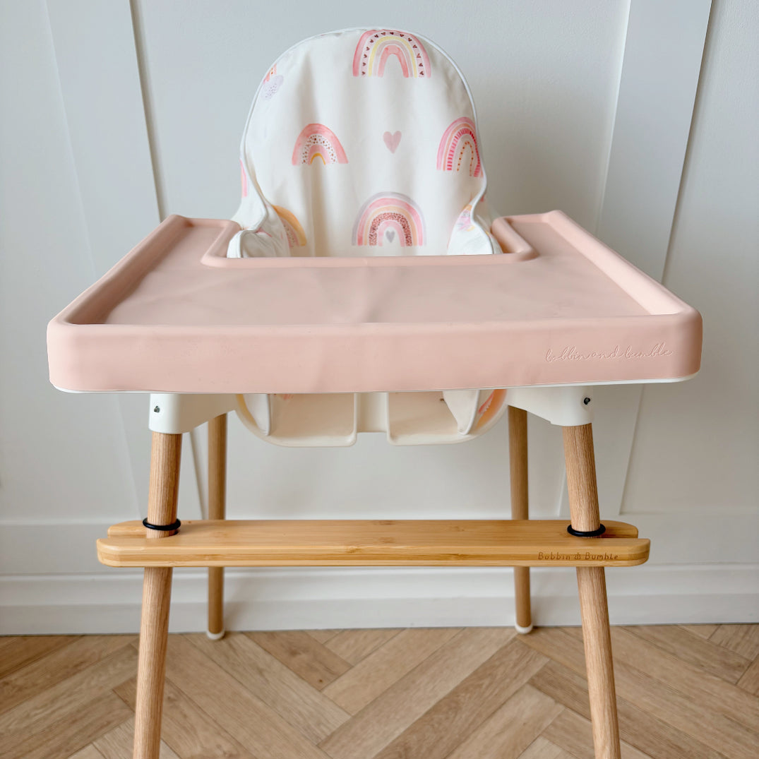 IKEA highchair with pale pink tray cover, cushion featuring rainbows against white wall