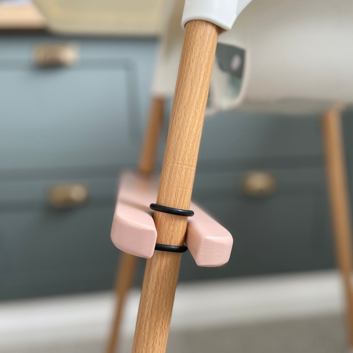 Side view of pink IKEA highchair footrest fitted on the leg of the highchair. Shows two o-rings either side