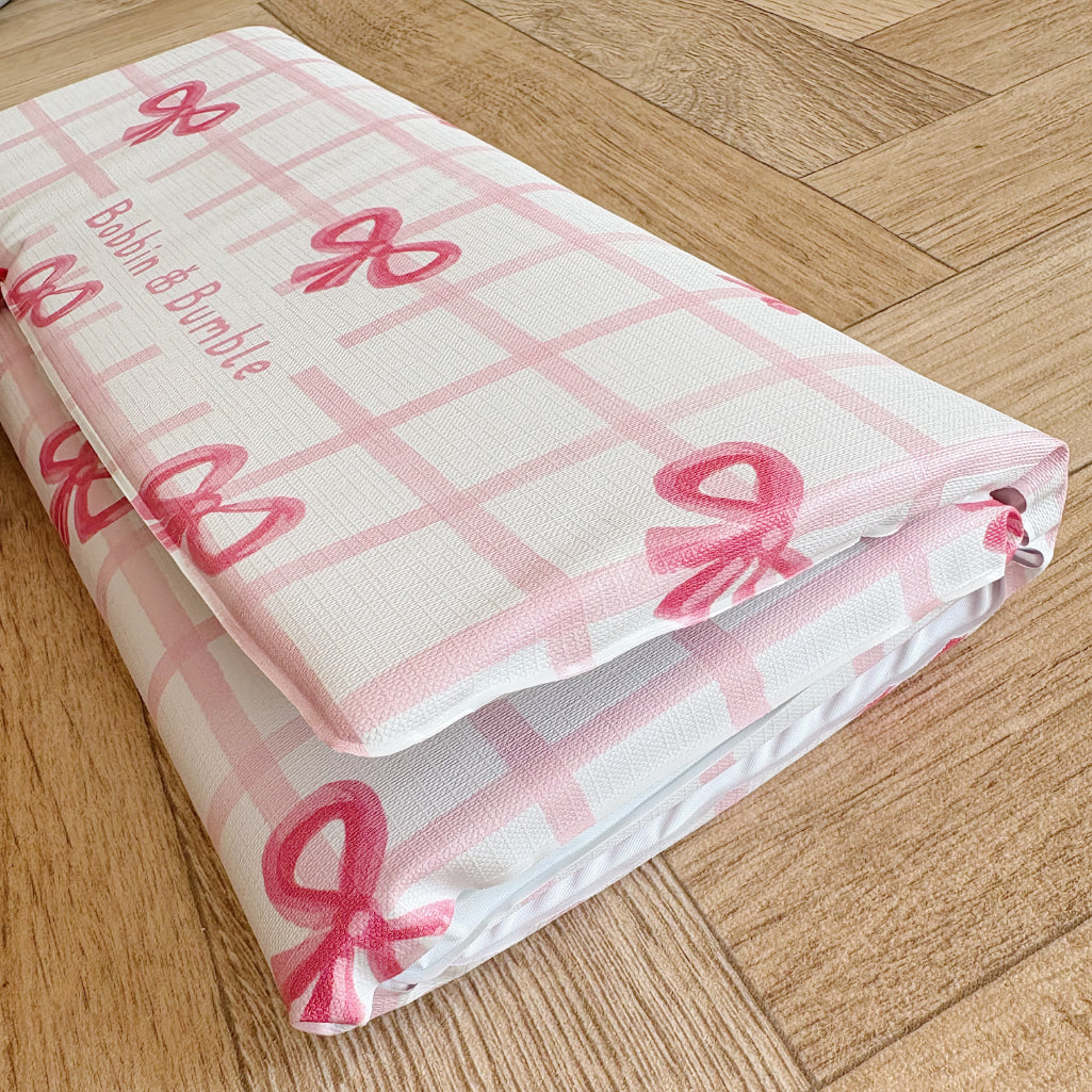 Pink checkered baby changing mat with bows on a wooden floor