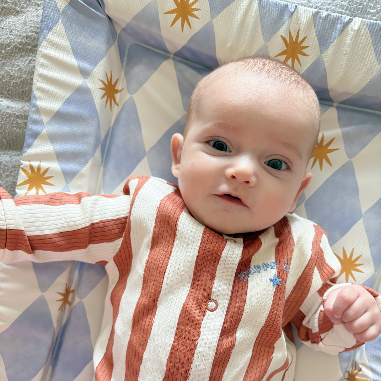 Baby in a brown striped onesie on a blue checkered changing mat