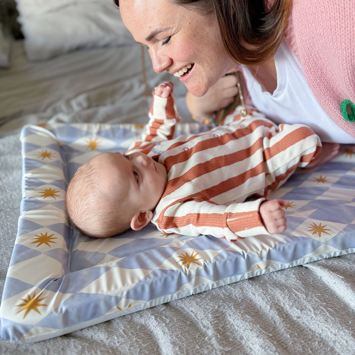 Baby on a blue checkered changing mat looking up at mum and smiling