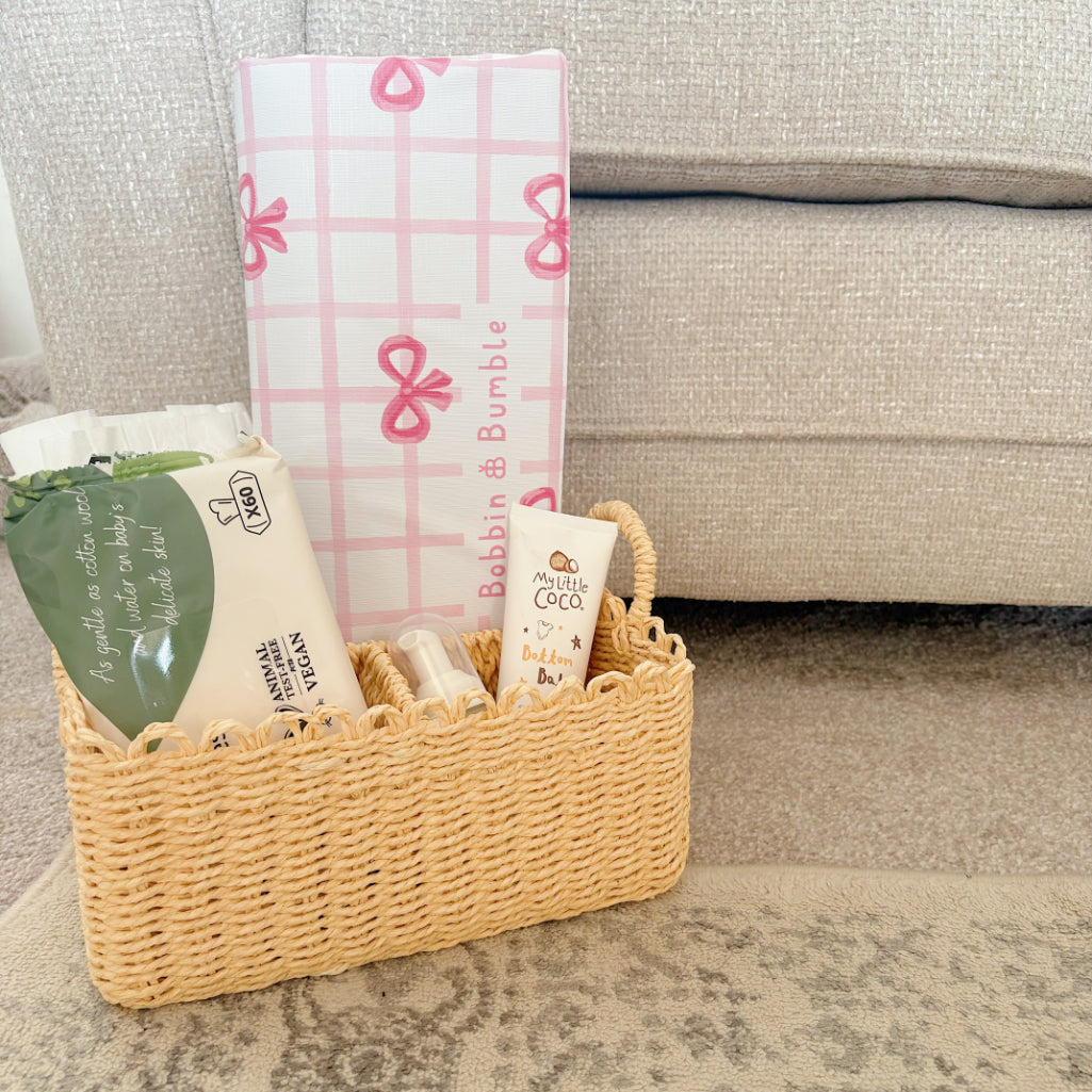 Wicker nappy basket with baby changing mat, wipes and cream on the carpet.