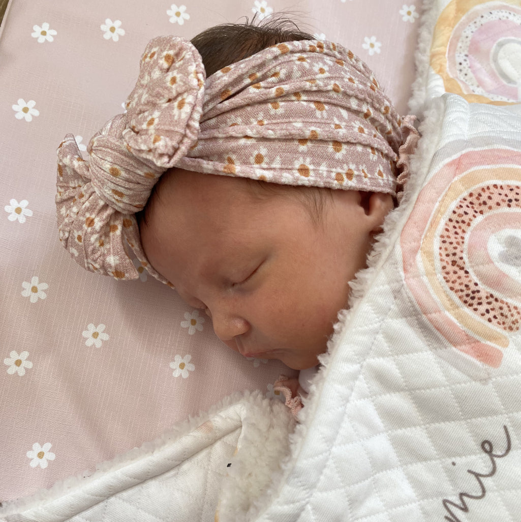 Baby sleeping on pink daisy changing mat with hair bow and blanket