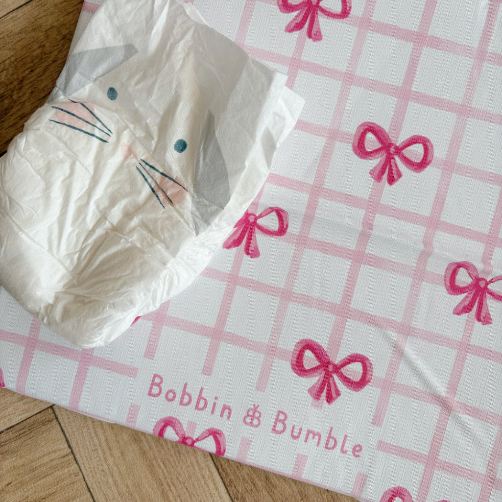 Disposable nappy on a pink checkered travel changing mat with red bows, featuring 'Bobbin Bumble' branding.
