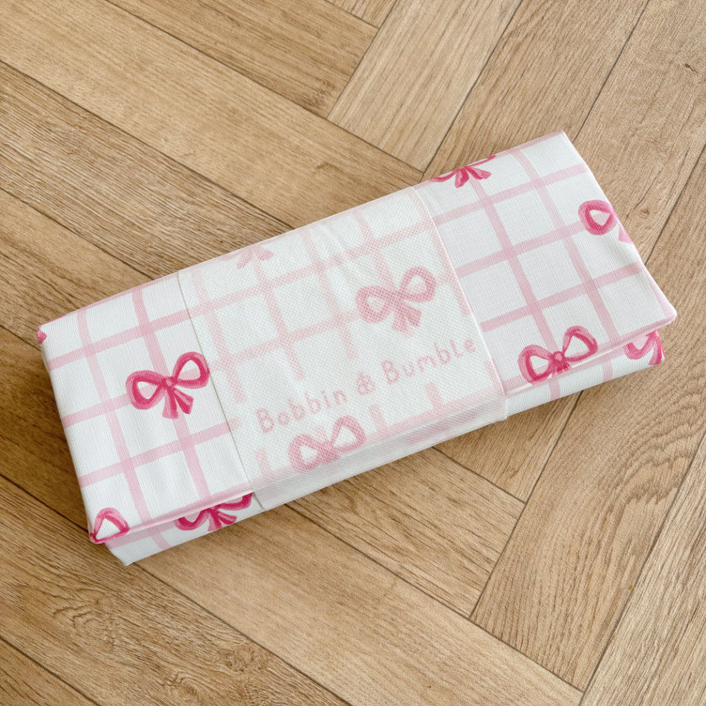 Folded baby changing mat with pink bows on a wooden floor