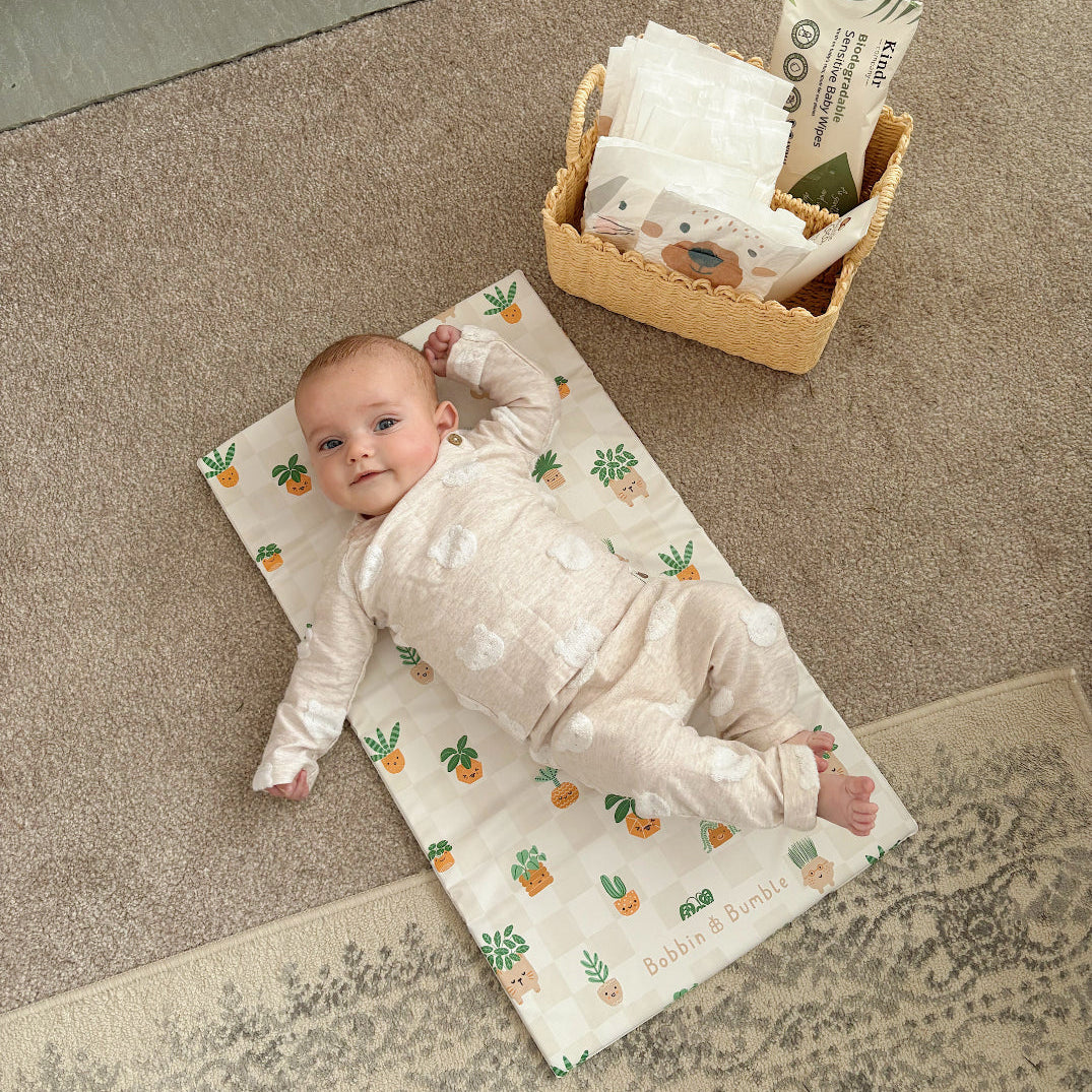 Baby lying on a patterned mat with a basket of diapers nearby