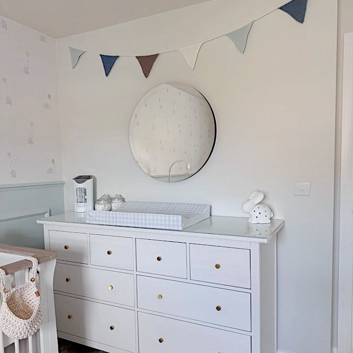 Nursery room with white dresser, crib, and decorative flags on the wall.