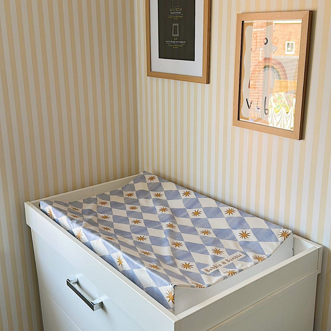 White dresser with a changing table cover in a room with striped wallpaper and framed pictures.