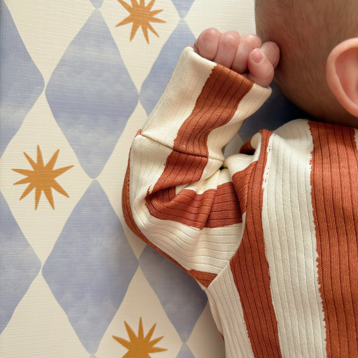 Close up of baby hand on a blue checkered changing mat.