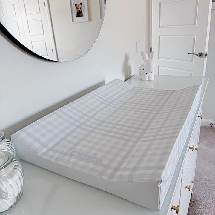 White bedroom with a large mirror on the wall and a wedge changing mat in blue gingham.