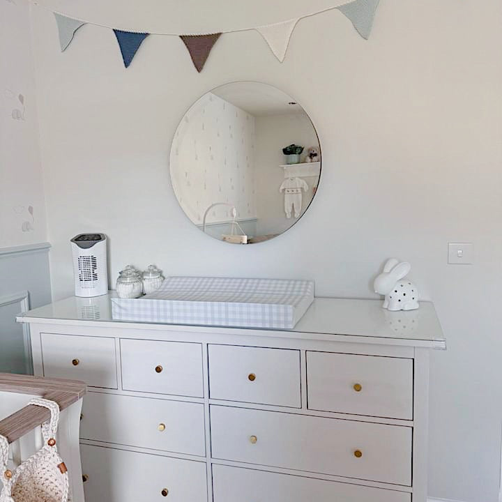 White dresser with round mirror and decorative flags in a baby nursery
