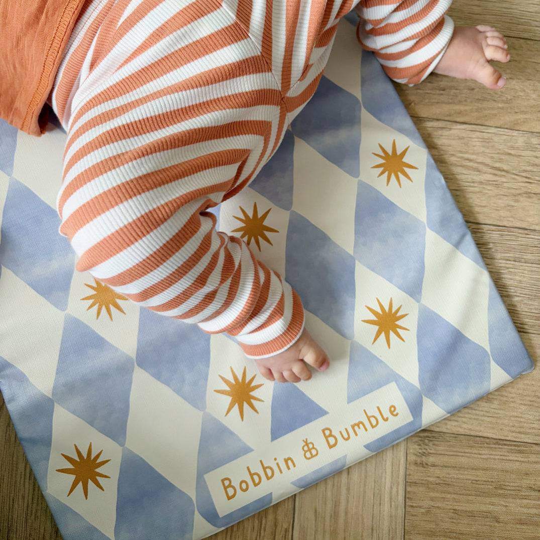 Child's legs in striped pants on a blue and white checkered mat with star patterns, branded 'Bobbin & Bumble'.
