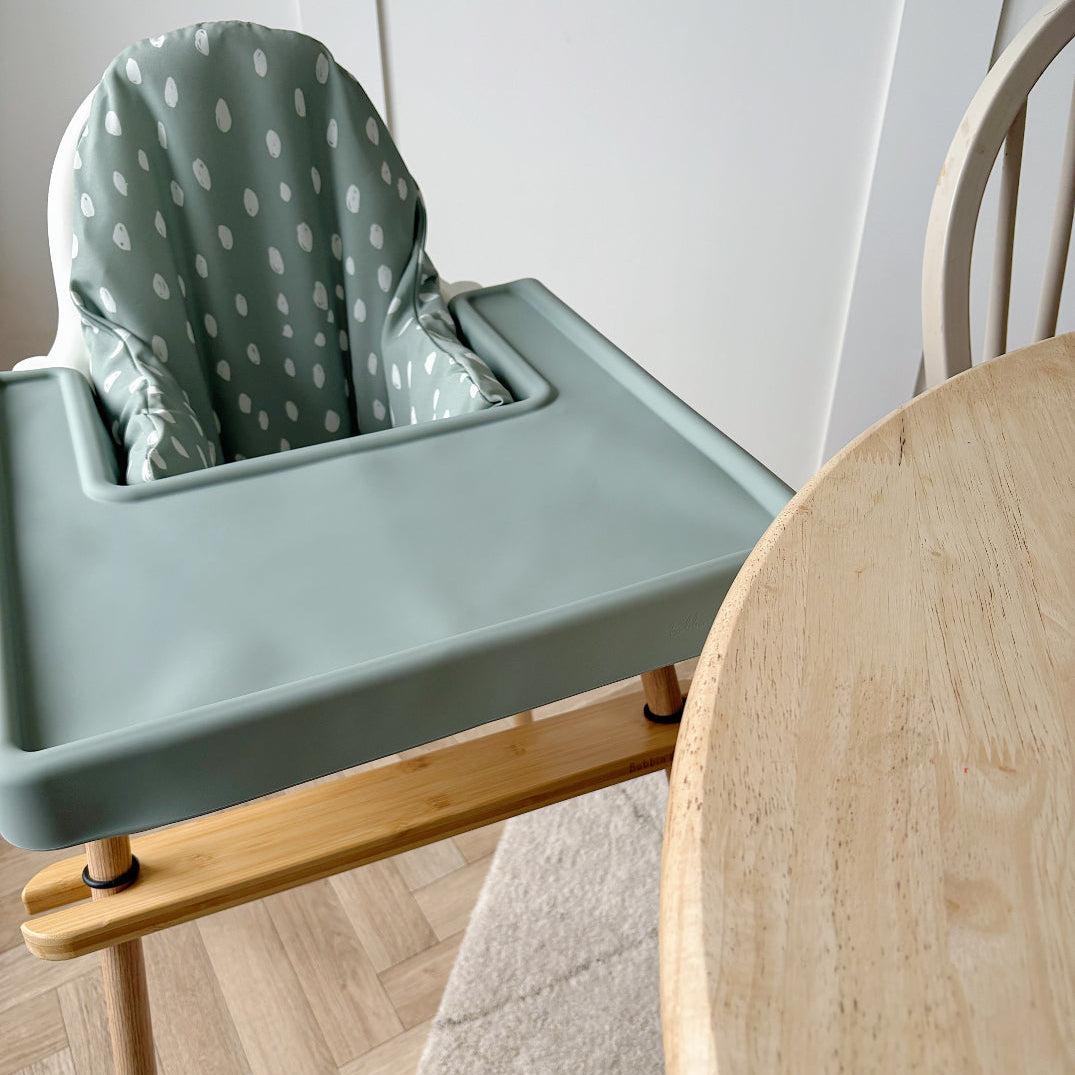 Green high chair with a polka dot cover on a wooden floor.