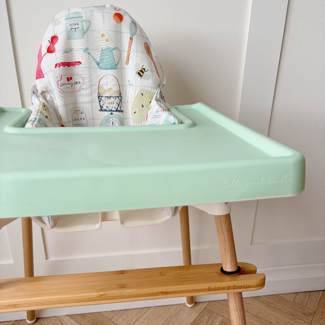 Mint green highchair tray with wooden legs on a wooden floor.
