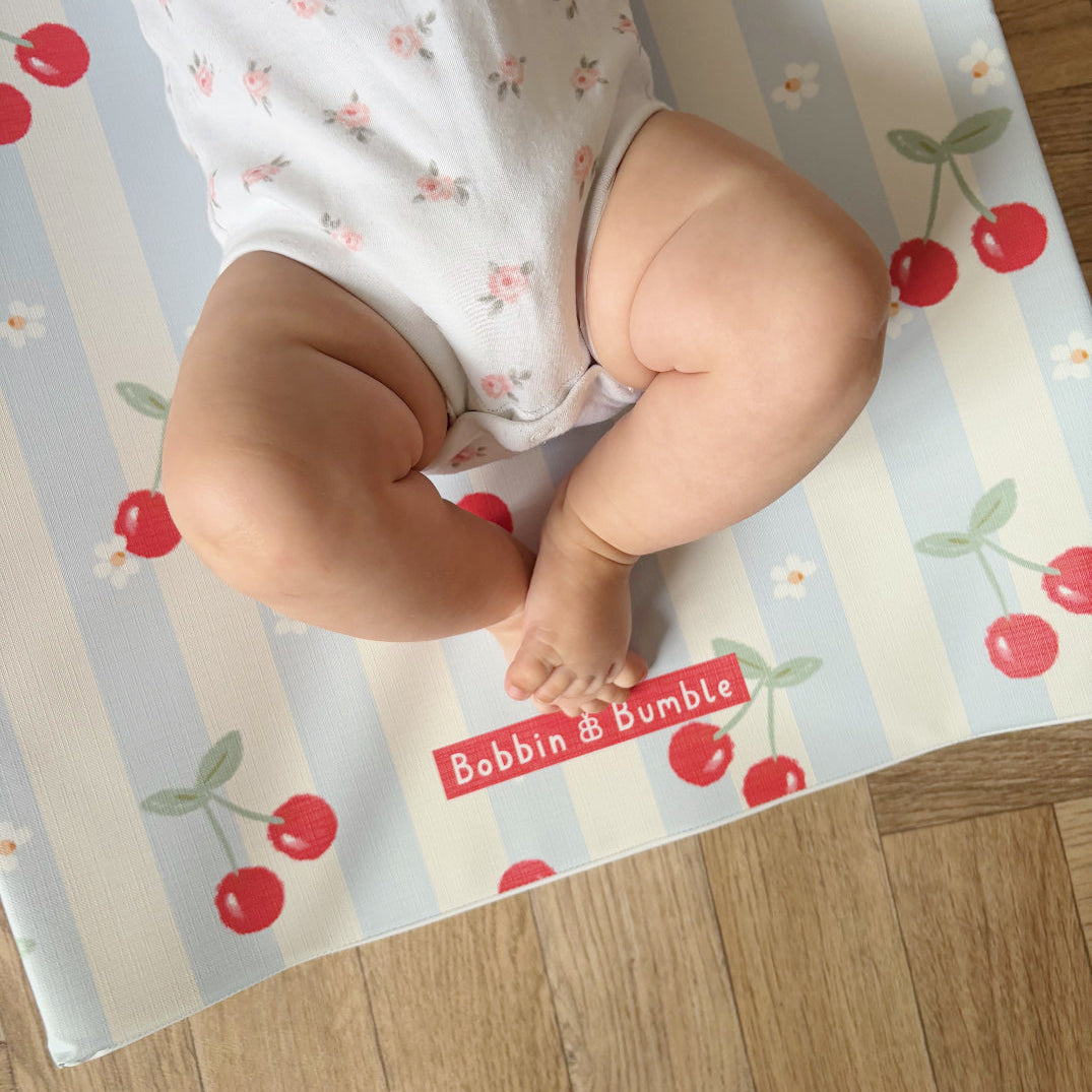 Baby legs on a play mat with cherry design and 'Bobbin & Bumble' branding.