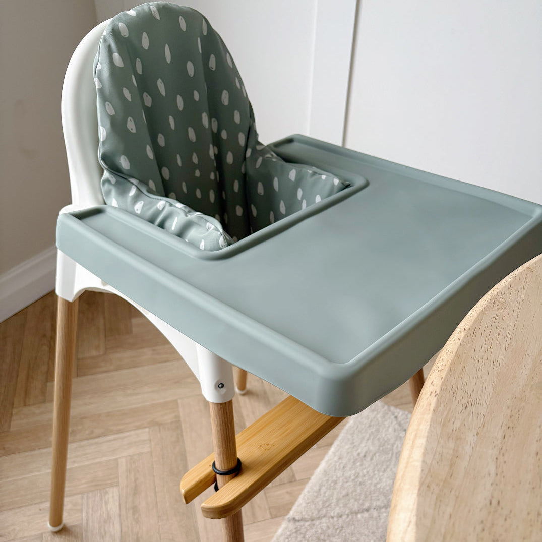 High chair with a green tray and white cushion on a wooden floor.