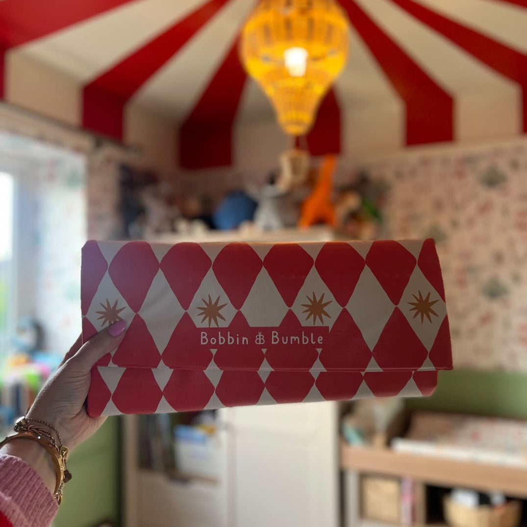 Red harlequin baby changing mat with Bobbin and Bumble branding held up against the circus themed nursery