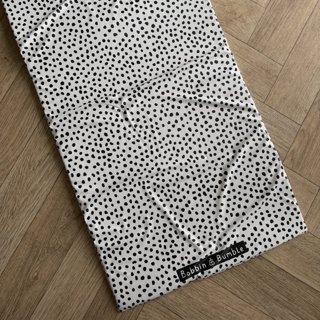 Black and white polka dot travel changing mat laid out on a wooden floor with 'Bobbin & Bumble' label.