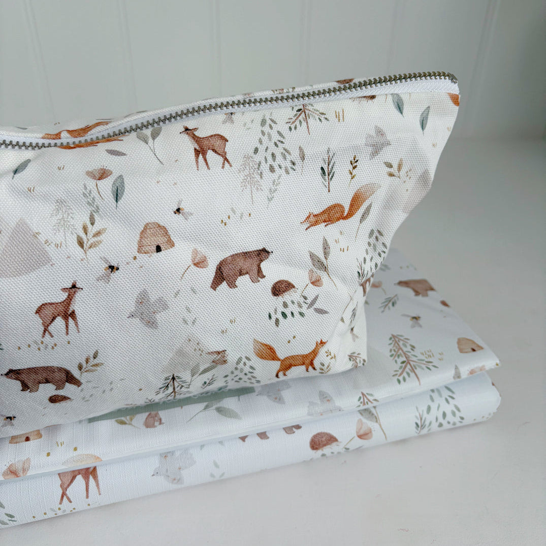 Folded travel baby changing mat with matching nappy wallet in a woodland animal pattern on a white surface