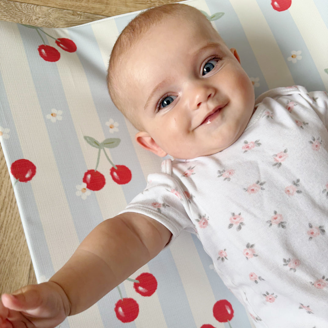 Baby in a white outfit with red cherry design on a striped background
