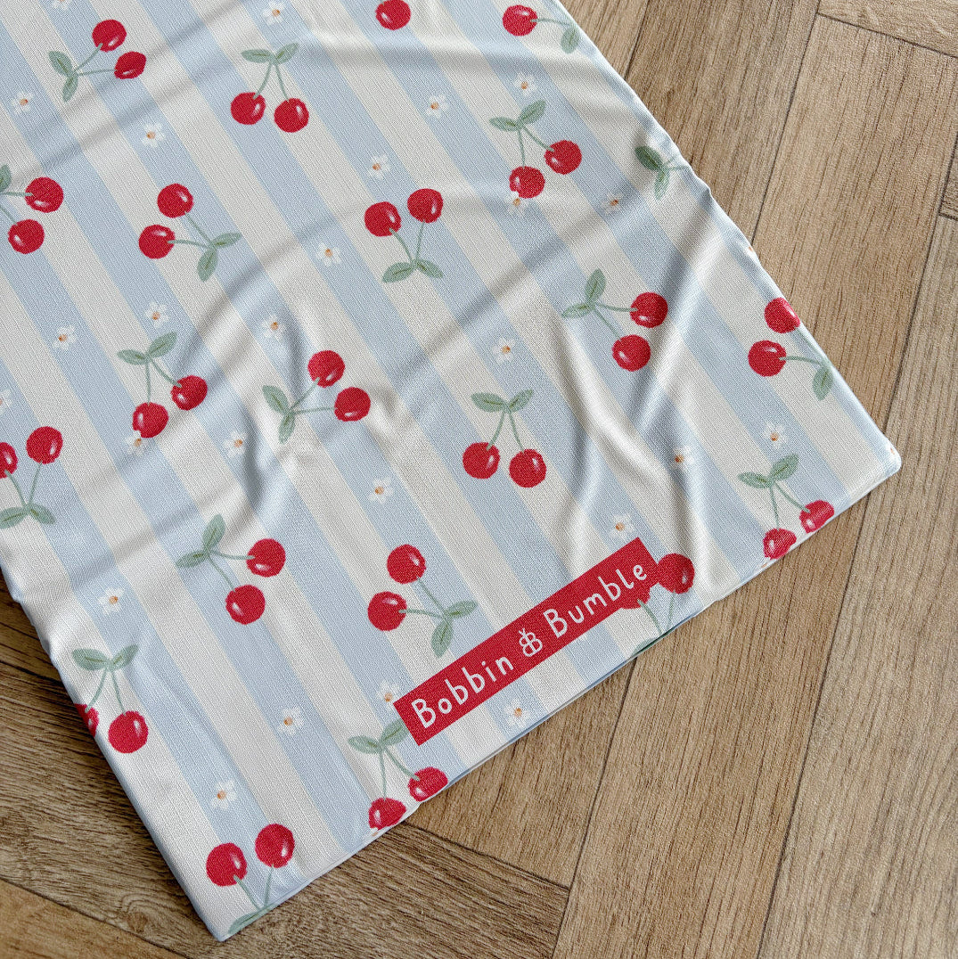 Travel changing mat with cherry pattern on a wooden surface, featuring the brand 'Bobbin & Bubble'.