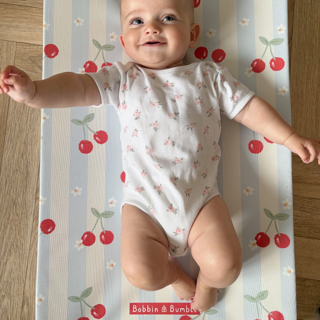 Baby lying on a cherry-patterned mat with 'Bobbin & Bumble' branding.
