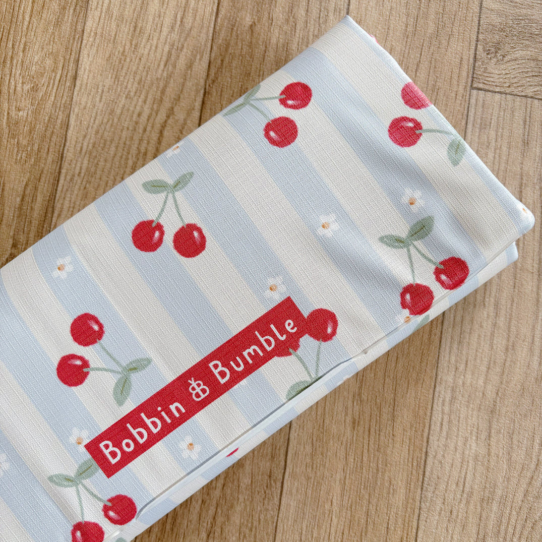 Folded changing mat with cherry pattern and 'Bobbin & Bumble' label on a wooden surface