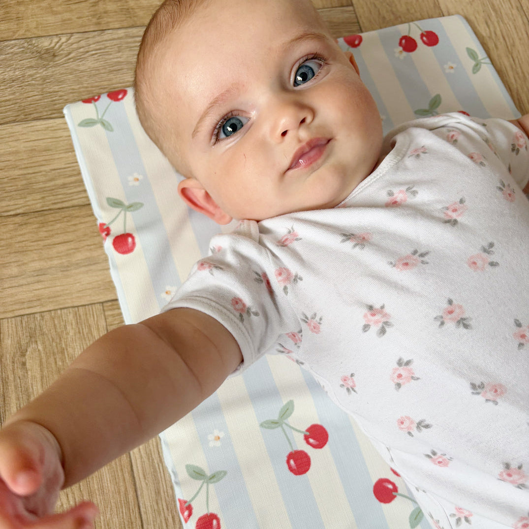 Baby lying on a cherry-patterned mat with a wooden floor background