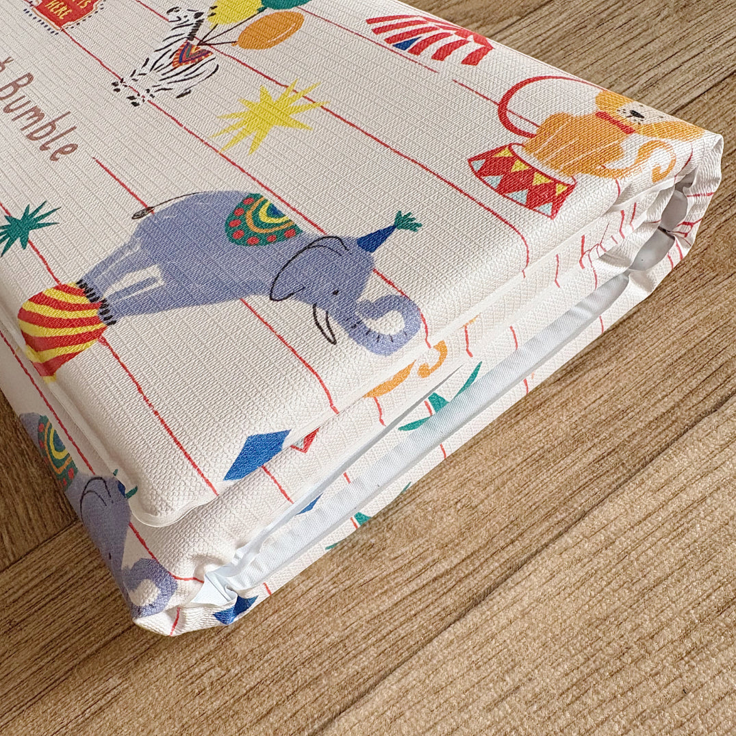 Folded travel changing mat with colourful circus design on a wooden surface