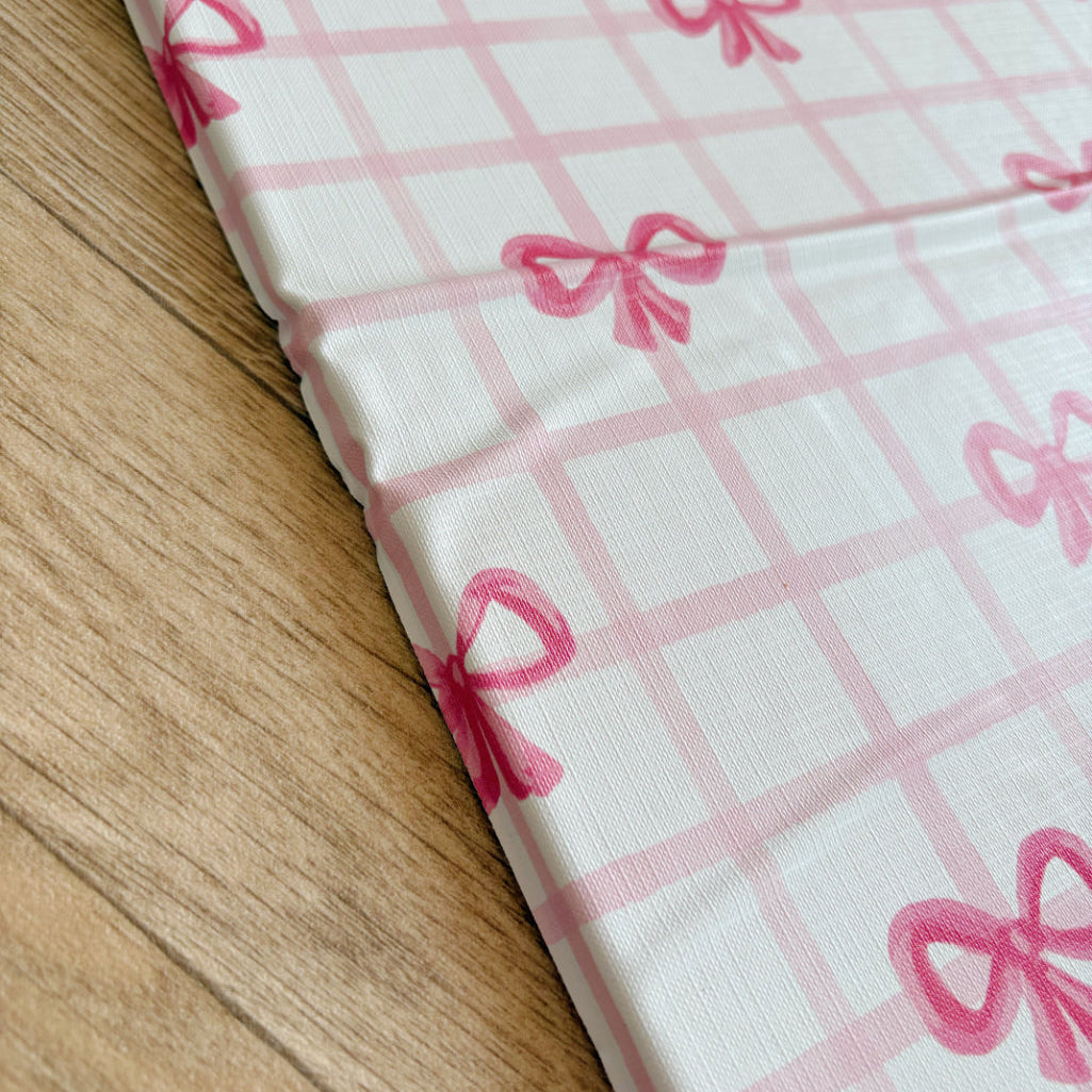 Travel changing mat with pink bow pattern on a white background, laid over a wooden surface.
