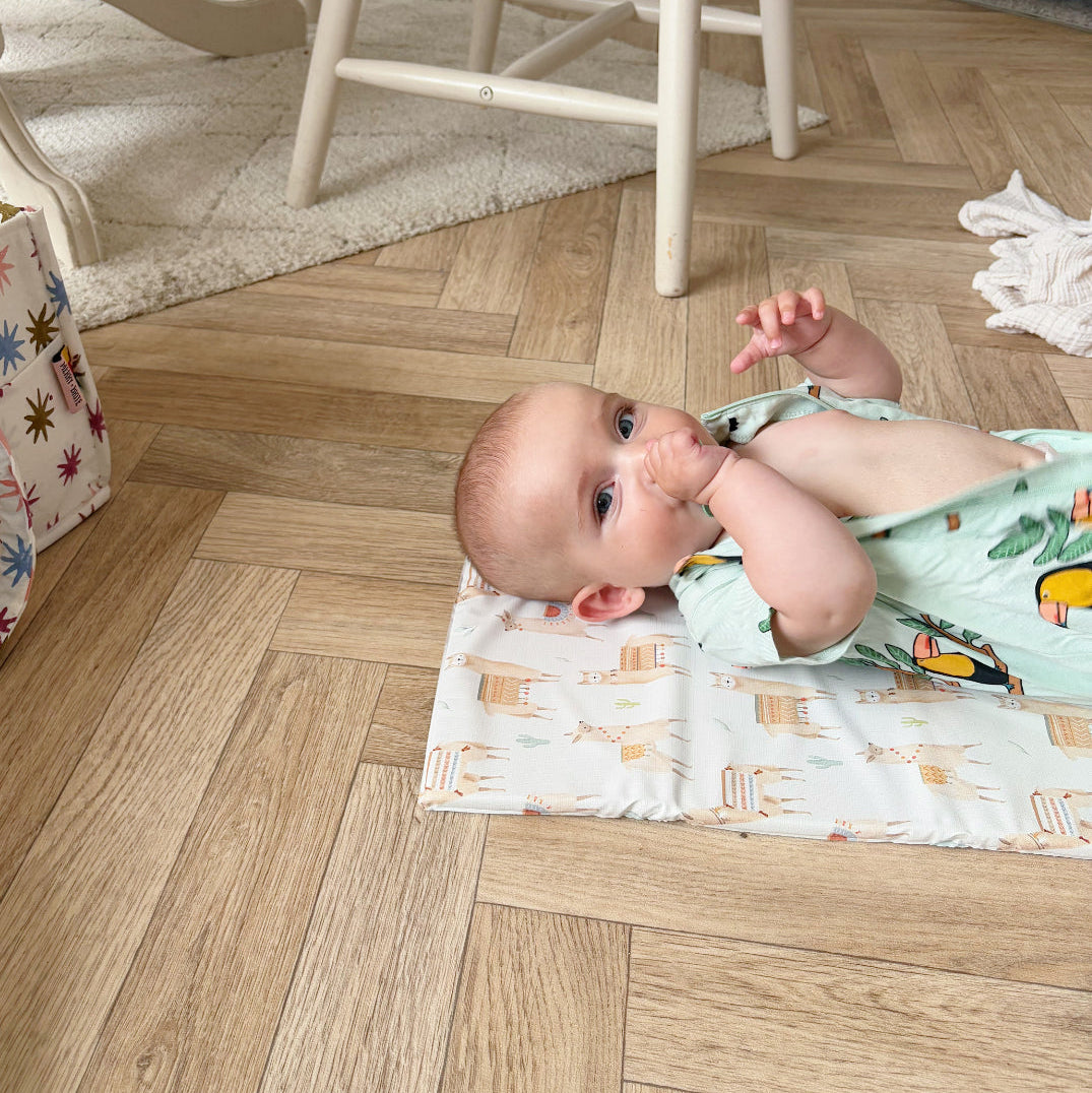 Baby lying on a wooden floor with a colorful changing mat