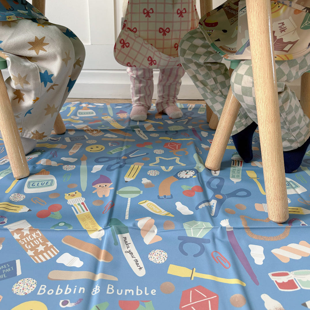 Children playing at a table, with a colorful patterned floor splash mat.