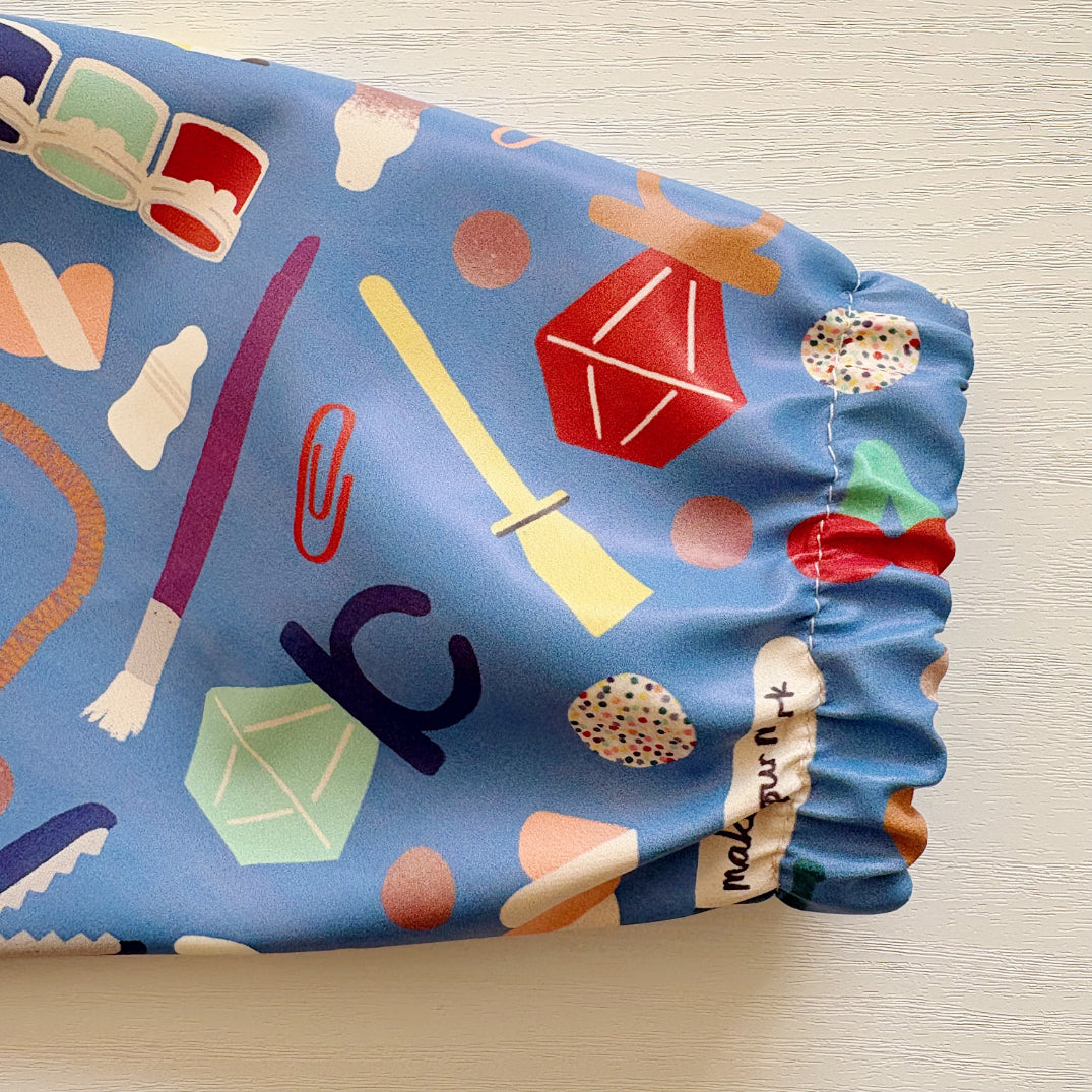 Close up of an elasticated sleeve cuff from a baby bib showing colourful fabric with various patterns on a light background