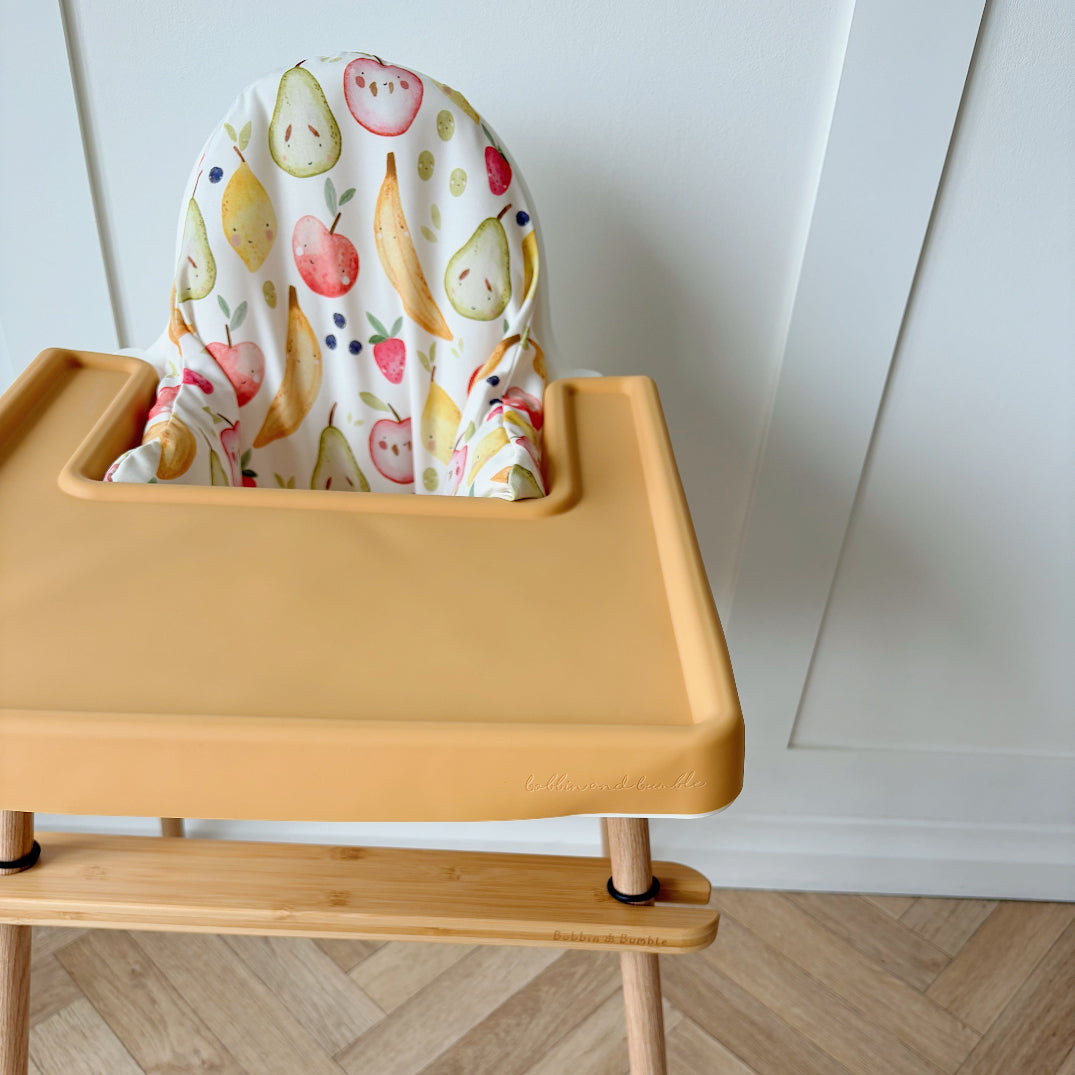 Yellow high chair with a colorful fruit-patterned cover on a wooden floor.