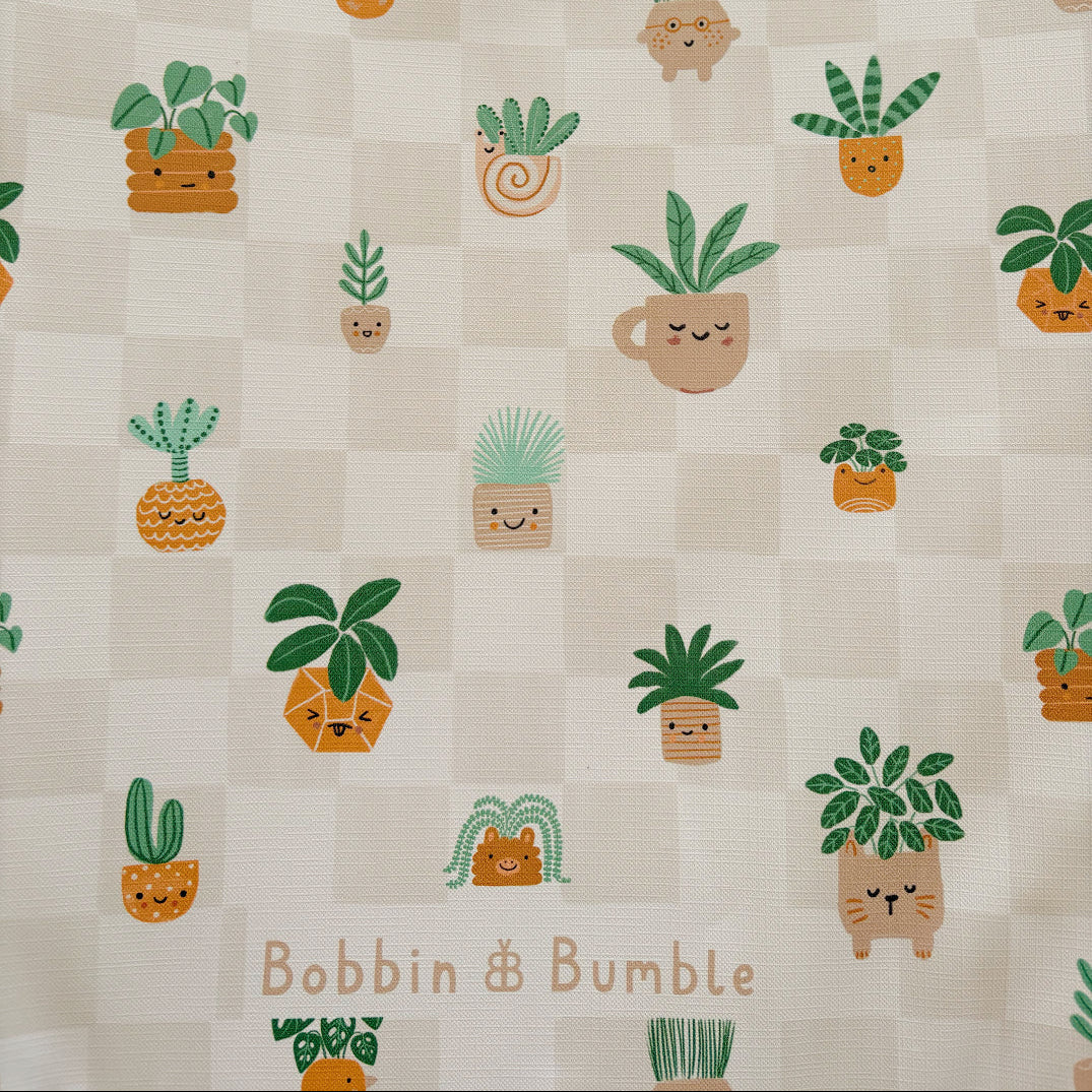 Pattern of cartoon plants with faces on a checkered background, featuring the brand 'Bobbin & Bumble'.