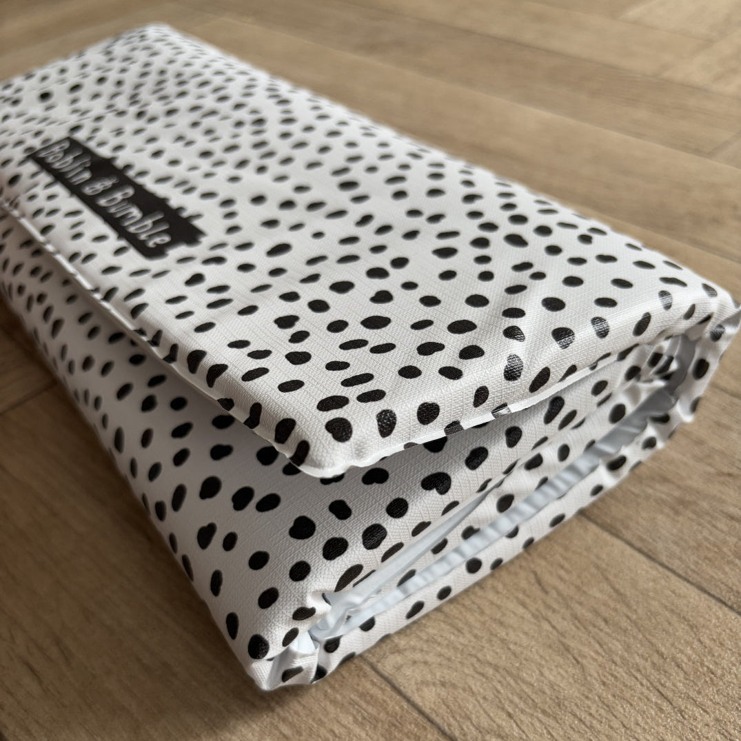 Folded polka dot travel baby changing mat with a Bobbin and Bumble label on a wooden floor