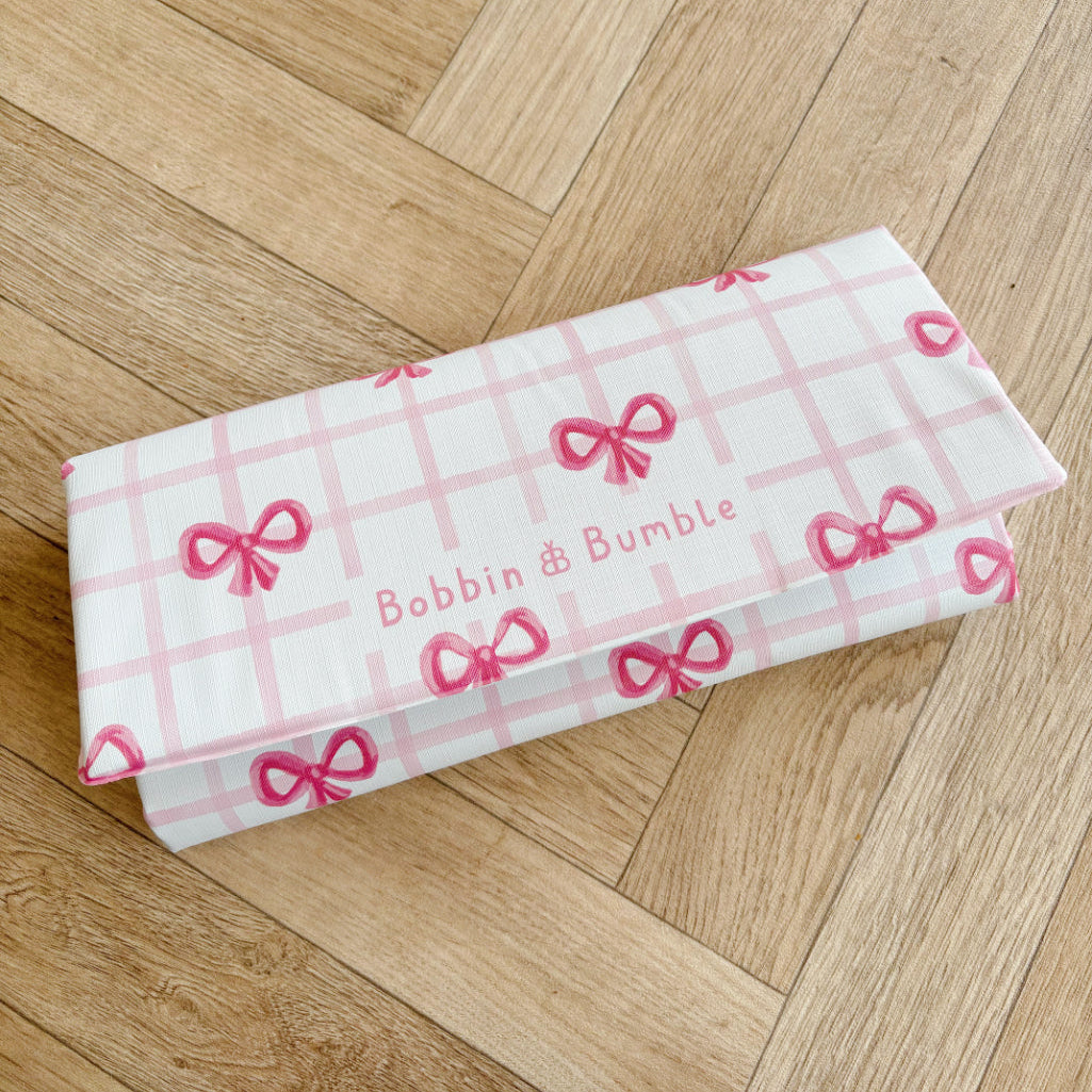Folded baby changing mat with pink bow pattern on a wooden floor