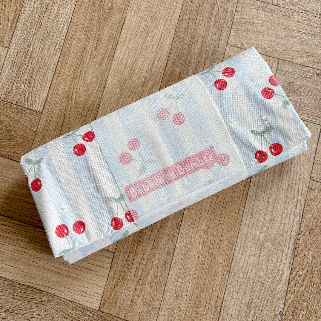 Folded travel changing mat with cherry pattern on a wooden floor