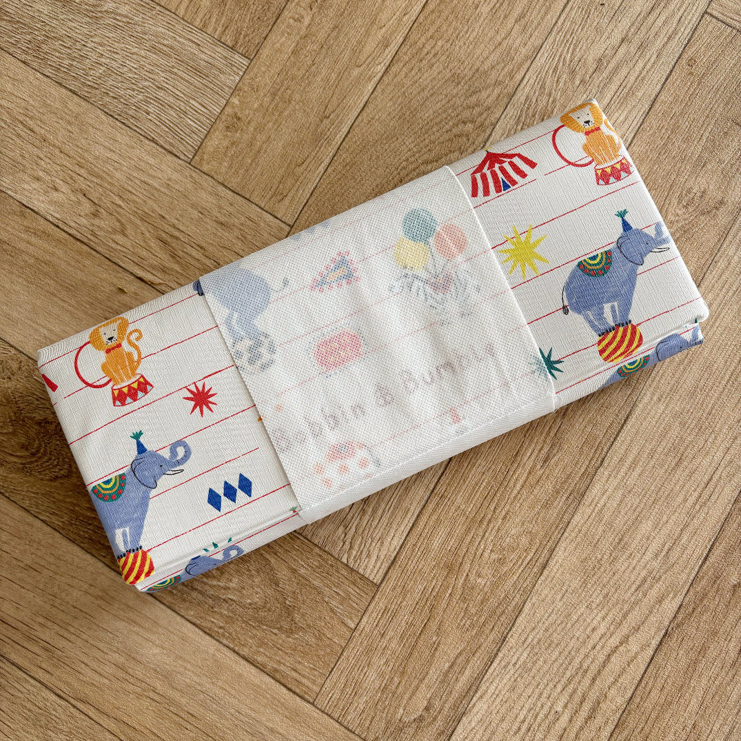 Children's travel baby changing mat with colourful circus animal illustrations on a wooden floor