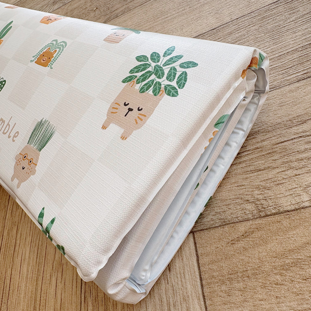 Folded travel baby changing mat with cartoon plant designs on a wooden floor.