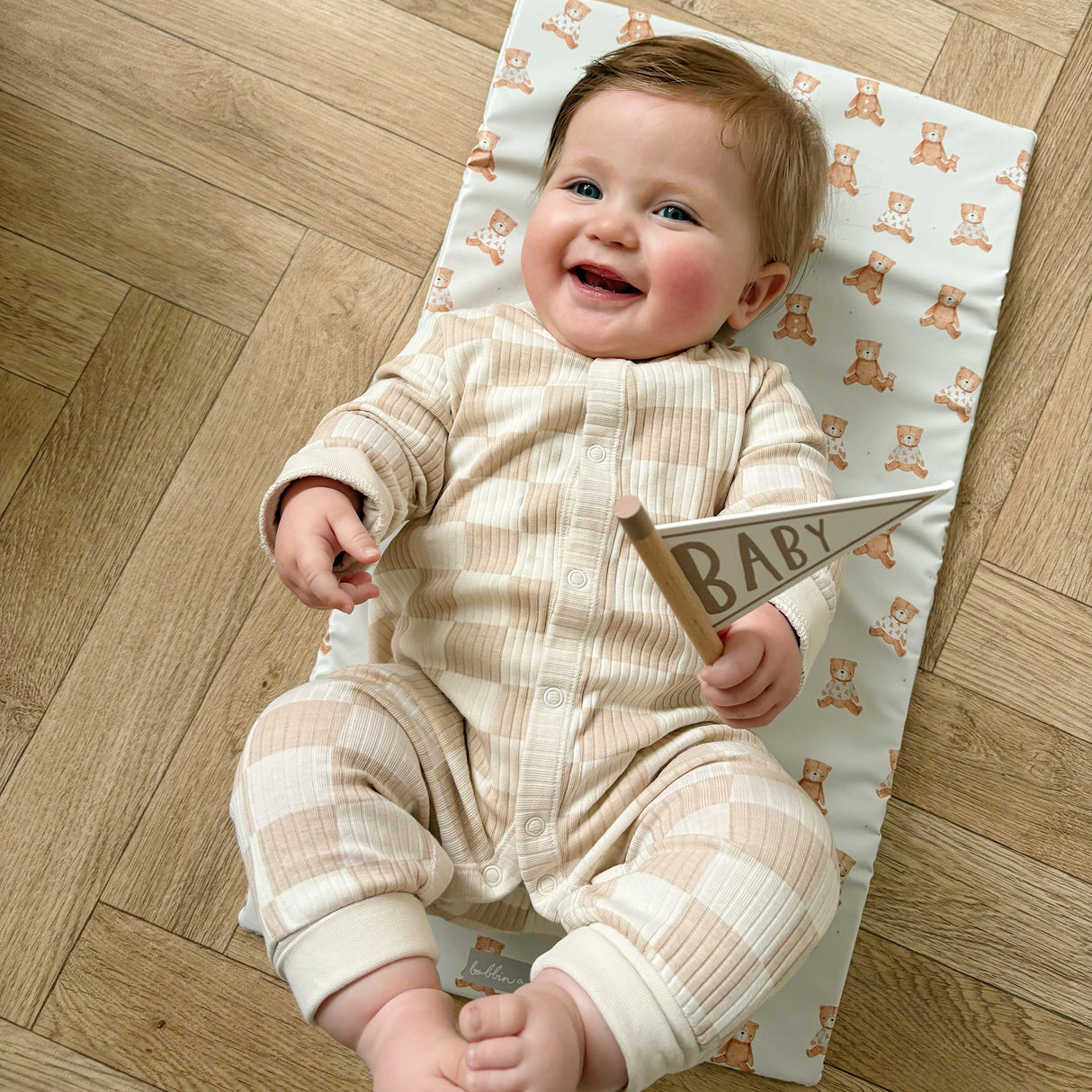 Baby smiling laying on a teddy bear print travel changing mat on wooden floor