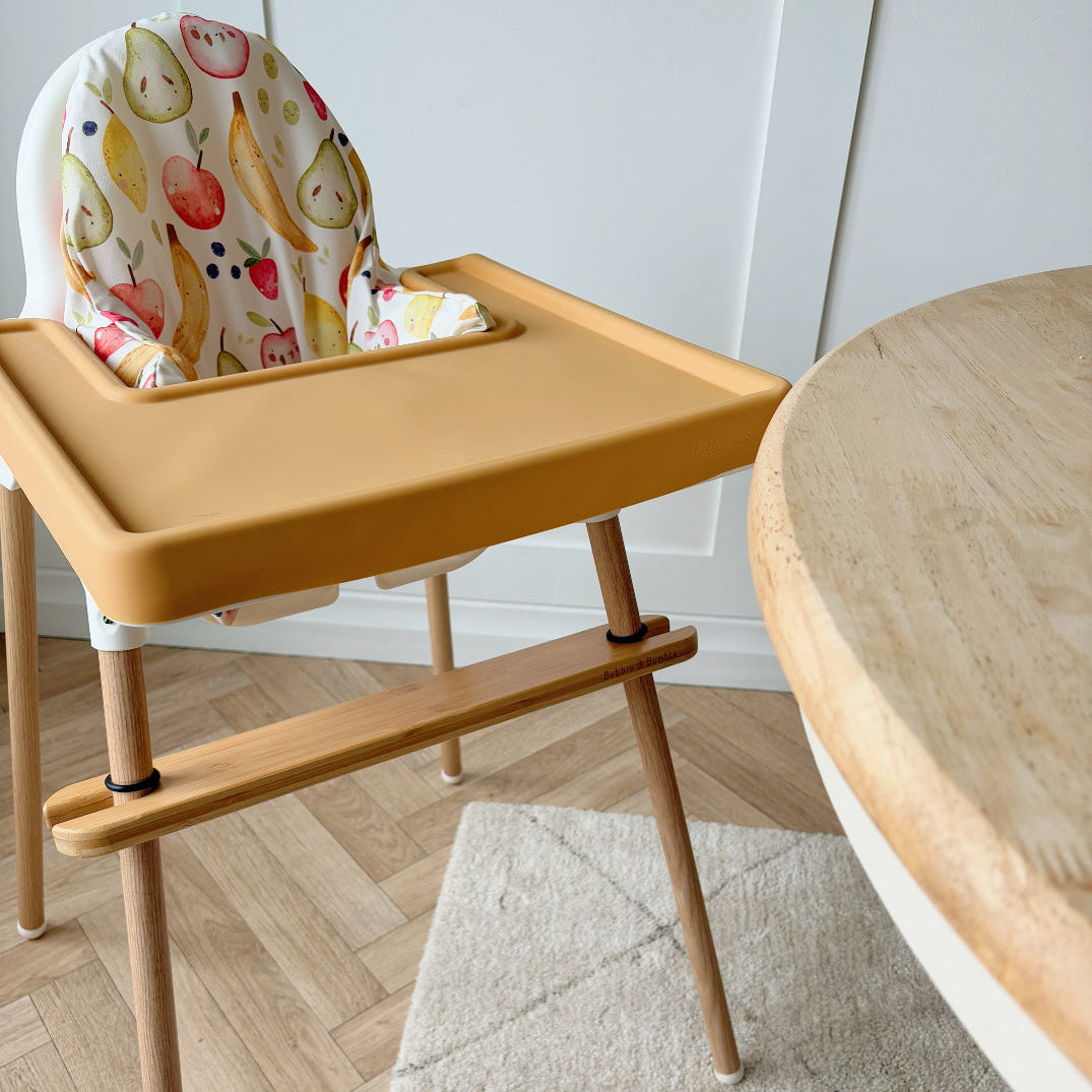 Wooden high chair with colorful seat cover on a wooden floor.