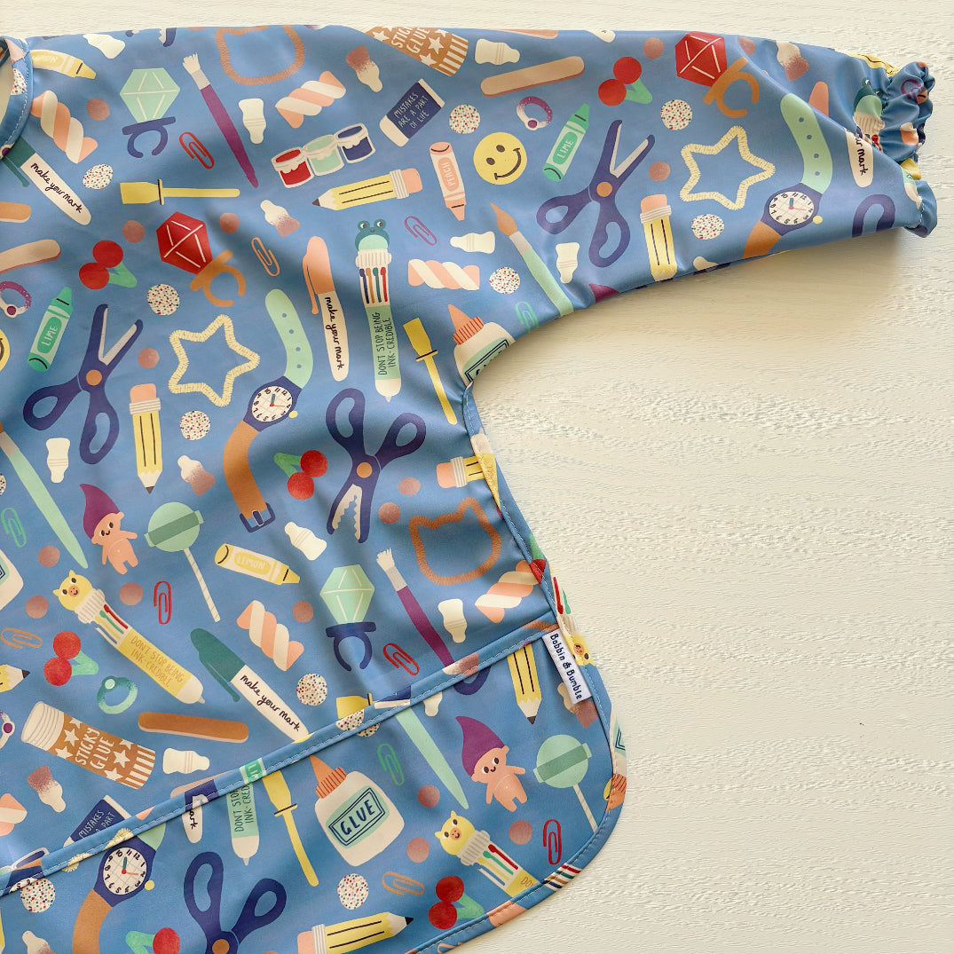 Blue long sleeved childrens bib with a colourful stationary design
