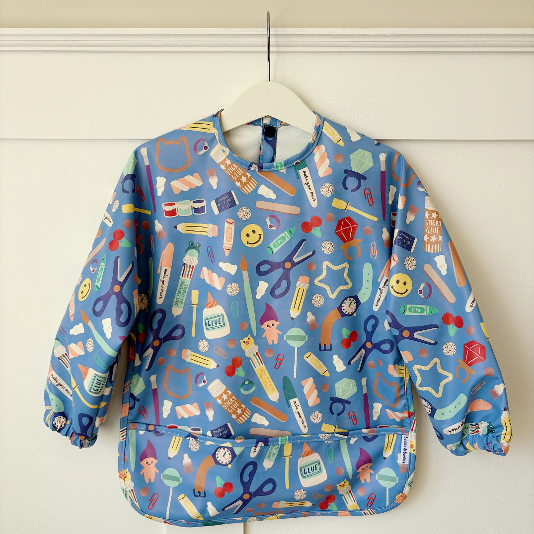 Children's blue long sleeved bib with a colourful stationery pattern on a white background