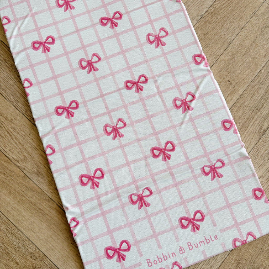 Laid out travel changing mat with pink bow pattern on a wooden floor